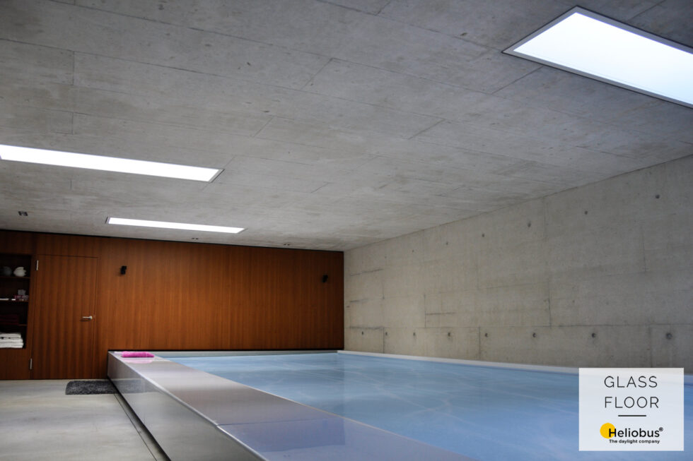 Přirozené osvětlení soukromého podzemního bazénu denním světlem pomocí pochozích světlíků umístěných na stropu z pohledového betonu.